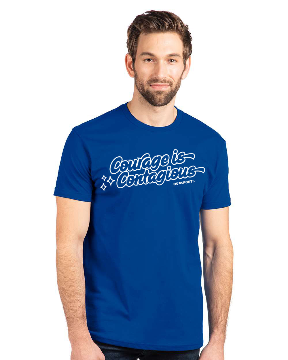 A man wearing a retro-style "Courage is Contagious" Outsports royal blue t-shirt with playful white script lettering and sparkle accents.